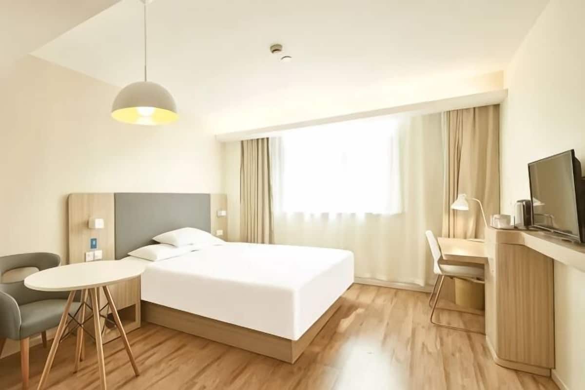 A hotel room with a bed, a desk, a chair, a TV, and a window with curtains.