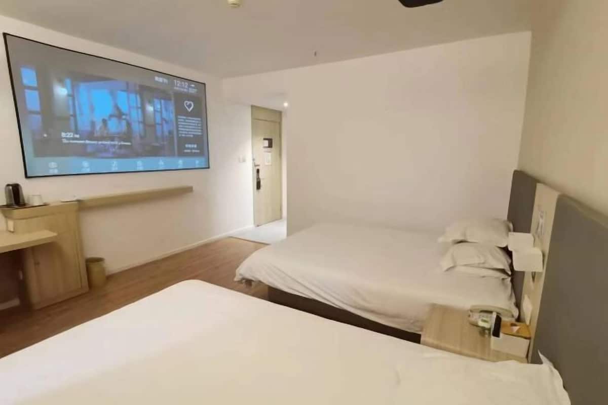 A hotel room with a bed, a desk, a TV screen, and a door.