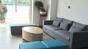 A modern living room with a grey sofa, a round coffee table, and a blue ottoman. There is a potted plant on a side table. - Jiangcheng Hotel (Wuhu Fangte Phase 2 Ocean Park) (Wuhu)
