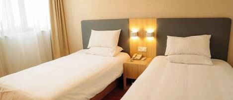 Habitación de hotel con dos camas individuales, una mesita de noche de madera con teléfono e iluminación empotrada.