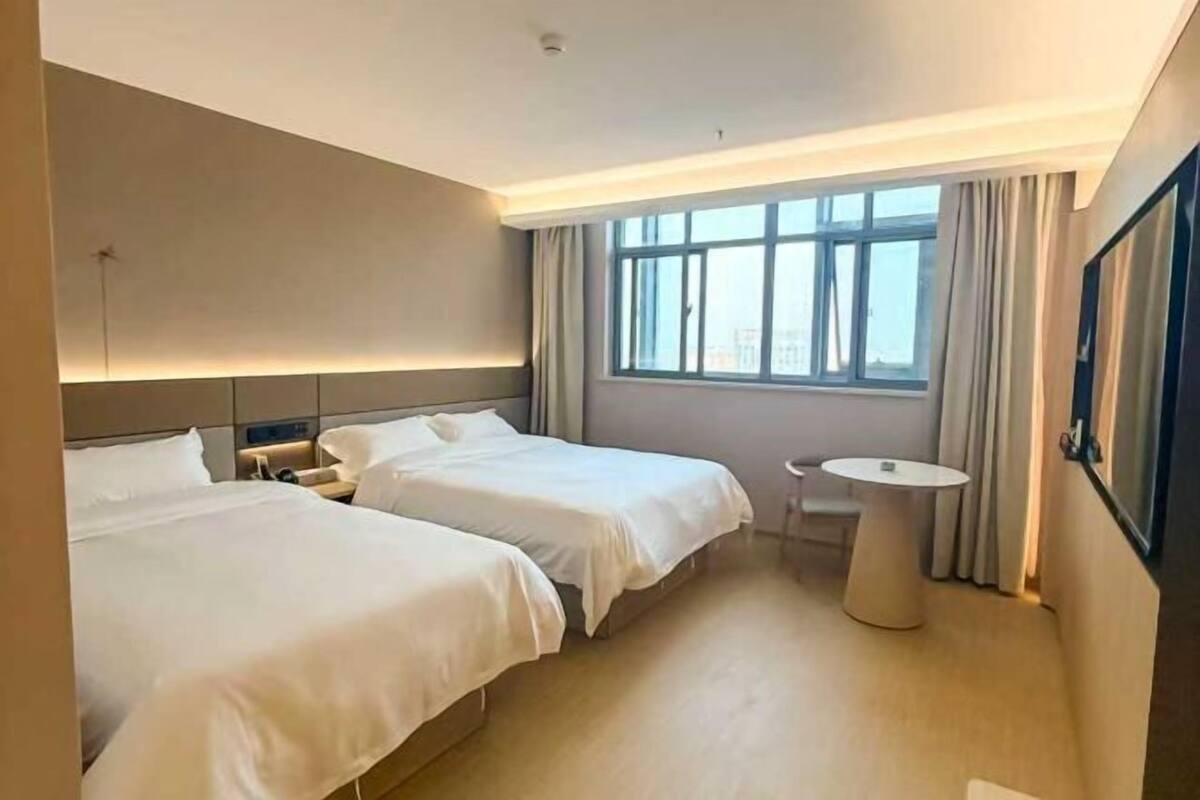 A hotel room with two beds, a small round table, and a window with curtains.