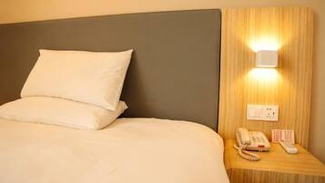 Habitación de hotel con cama, mesita de noche con teléfono y control remoto, y lámpara fijada a la pared.