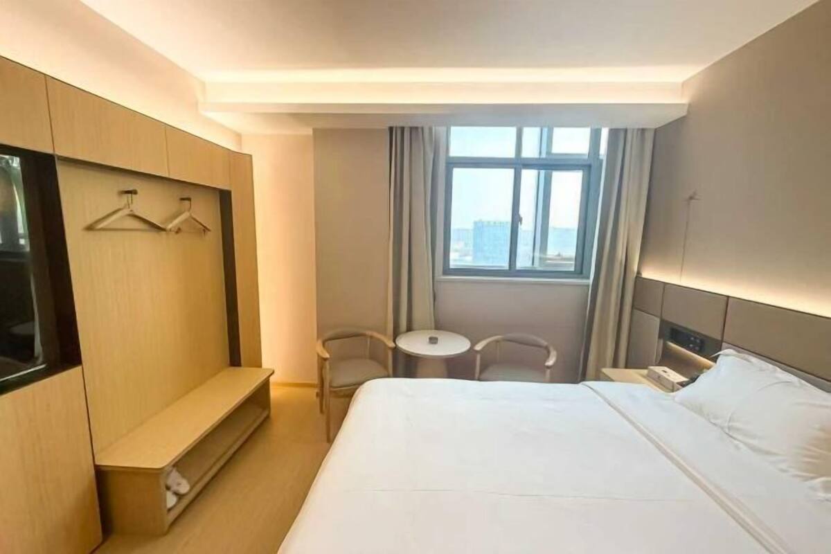 A hotel room with a bed, a seating area with two chairs, a small table, a TV mounted on the wall, and a window with curtains.