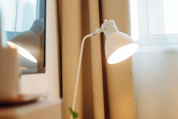 En hvid skrivebordslampe med fleksibel led, placeret ved et vindue med beige gardiner.