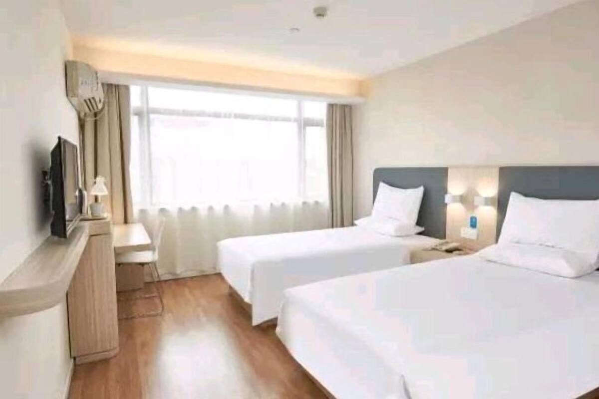 A hotel room with two beds, a desk, a TV, and a window with curtains.