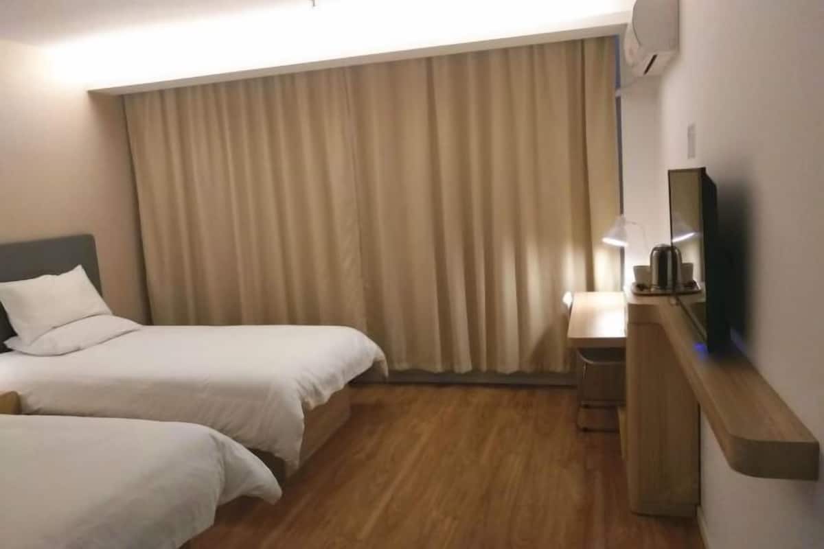 A hotel room with two beds, a desk, a chair, a TV, and a window with curtains.