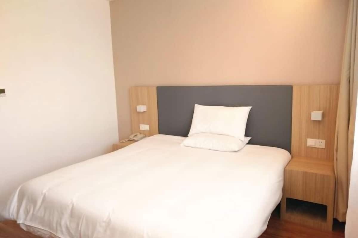 A neatly made bed with white linens, a grey headboard, and wooden nightstands with a phone and light switch.