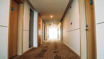 Un pasillo de hotel con puertas de madera, pisos alfombrados y un largo acceso a un extremo luminoso.