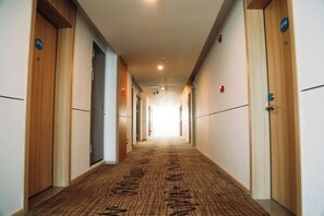 A hotel corridor with wooden doors, carpeted floors, and a long hallway leading to a bright end. - Jiangcheng Hotel (Wuhu Fangte Phase 2 Ocean Park) (Wuhu)