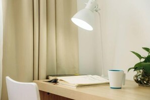 Et skrivebord med en hvid lampe, en plante og en kop.