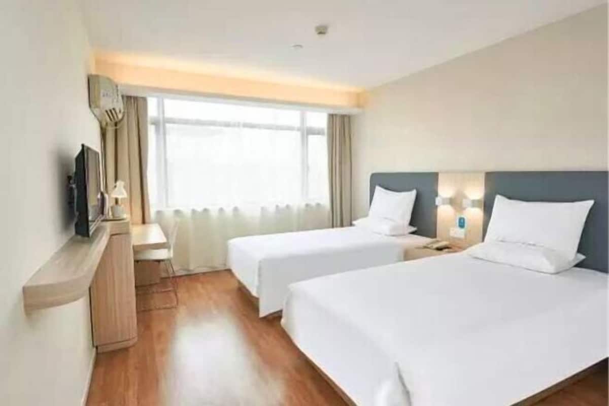A hotel room with two beds, a desk, a TV, and a window with curtains.