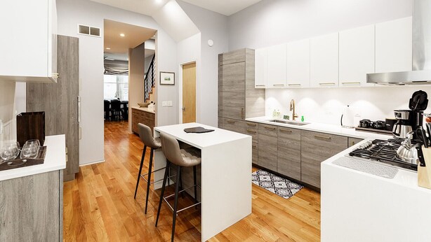 Una cocina moderna con armarios blancos, una isla central con taburetes y un comedor al fondo.