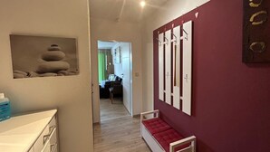 A hallway with a bed, a red wall, and a painting of stacked stones.