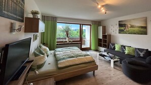 A modern bedroom with a bed, a TV, a sofa, and a view of the outdoors.