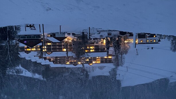 A snow-covered landscape with buildings reflecting on a calm body of water.