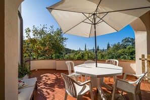 Un patio con mesa y sillas, una sombrilla y vistas a árboles y colinas.