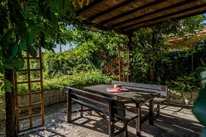 Eine Außenpatio mit Holzbänken und einem Tisch, umgeben von üppigem Grün und einer Steinmauer.