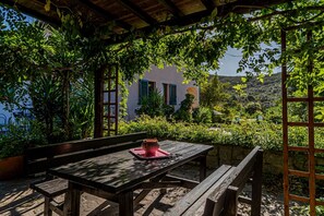 Ein Holztisch mit einer roten Tablettablage unter einer mit Kletterpflanzen bewachsenen Pergola, mit Blick auf einen Hügel.