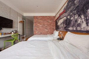 Habitación de hotel con una cama, un escritorio con una silla, un cuadro grande en la pared y una pared decorativa de ladrillo.