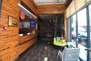 A reception area with a wooden interior, a reception desk, a seating area with a yellow chair, and a view of the parking lot through large windows. - Tuke China Hotel (Pingyang Aojiang Pearl Plaza Store) (Pingyang)