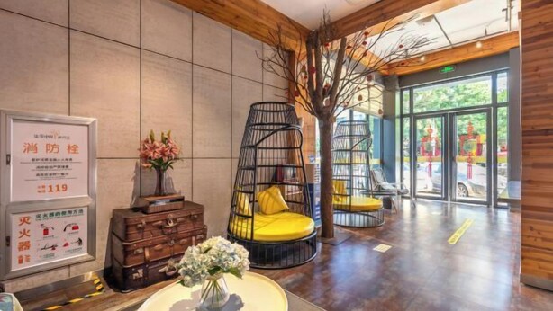 A modern lobby with a wooden ceiling, a reception desk, a decorative tree, and a seating area with a yellow chair. - Tuke China Hotel (Pingyang Aojiang Pearl Plaza Store) (Pingyang)