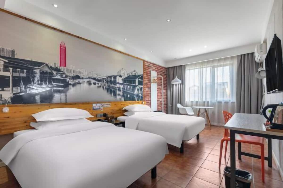 A hotel room with two beds, a dining table, a TV, and a mural of a cityscape.