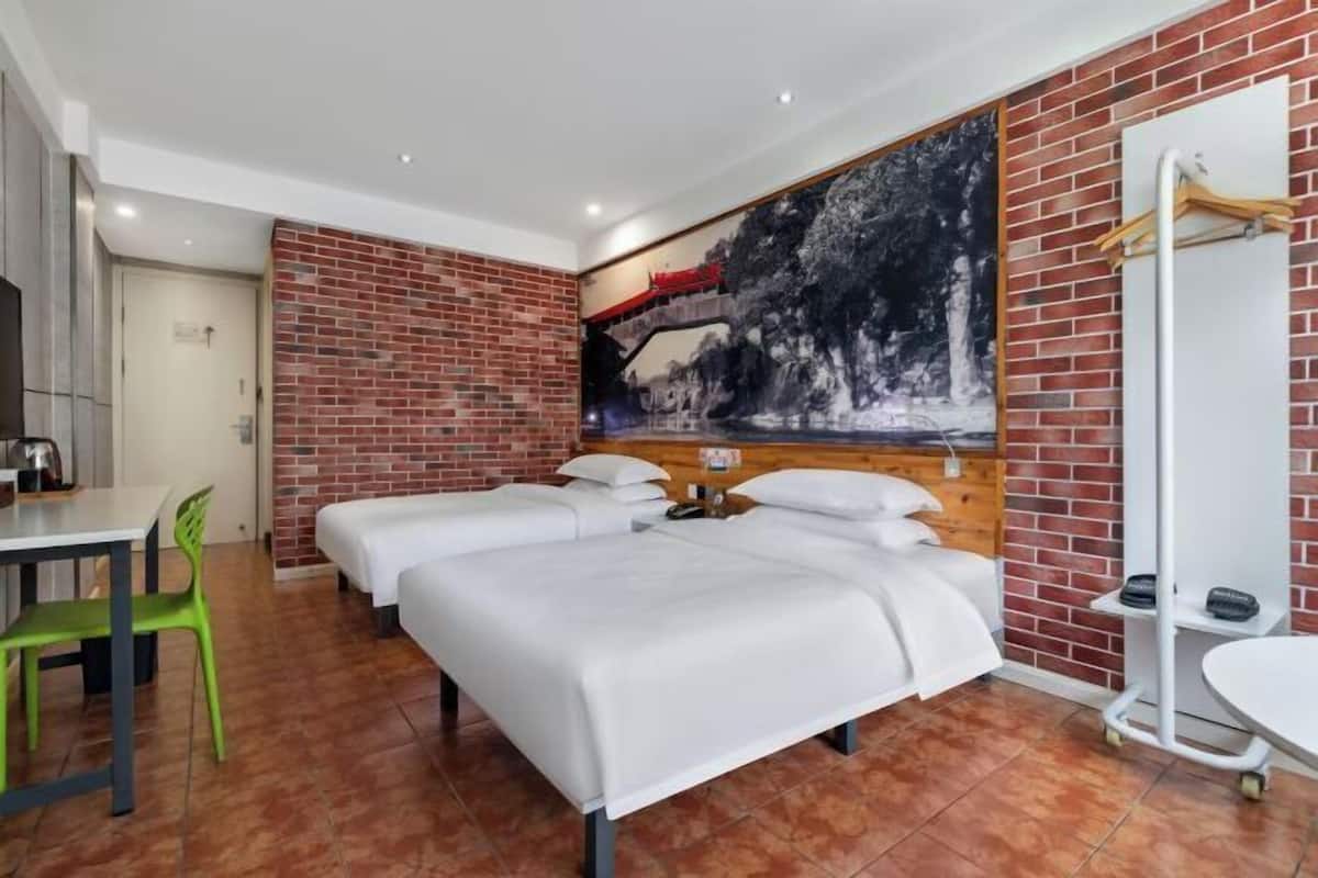 A hotel room with a brick wall, a large painting, two beds, a desk, and a chair.