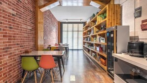 A modern interior with a brick wall, wooden ceiling beams, a long table with colorful chairs, and a bookshelf with various items. - Tuke China Hotel (Pingyang Aojiang Pearl Plaza Store) (Pingyang)