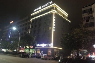 Un hotel con un letrero llamativo, varios pisos y un estacionamiento lleno de coches.