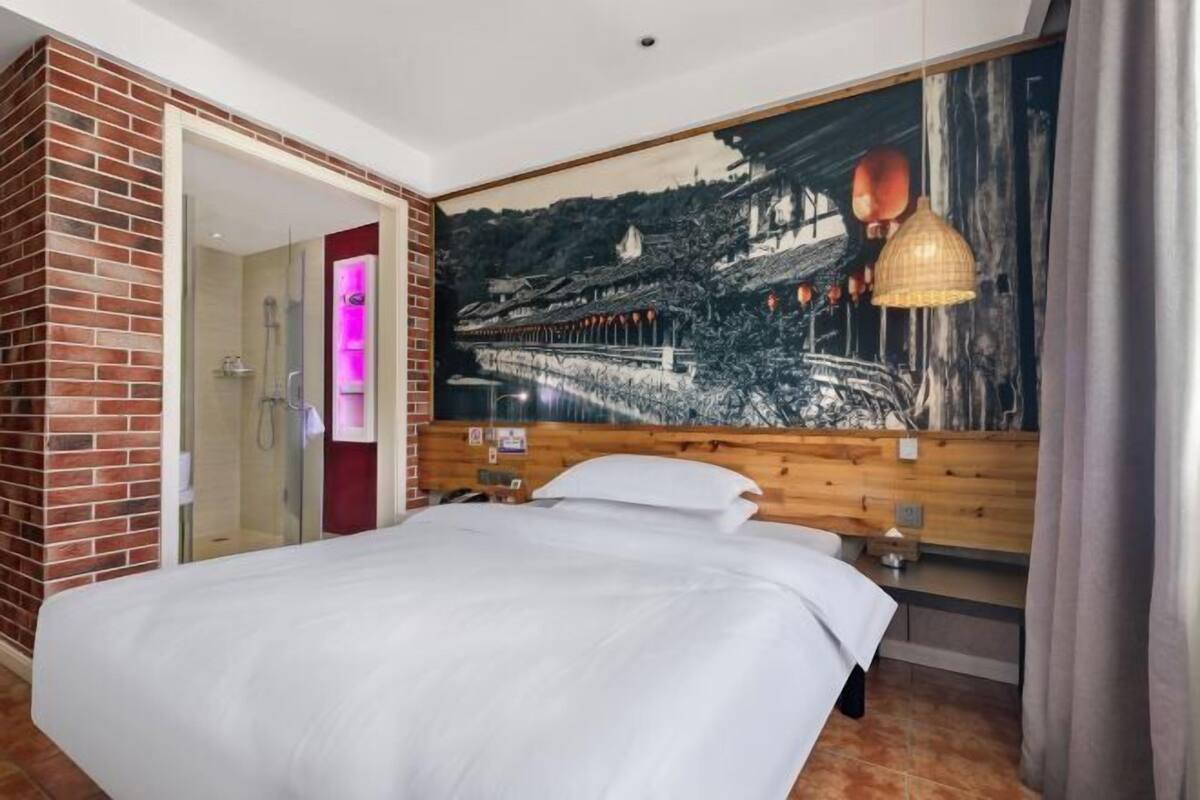 A hotel room with a large bed, a wooden headboard, a mural of a traditional bridge, and a brick wall.