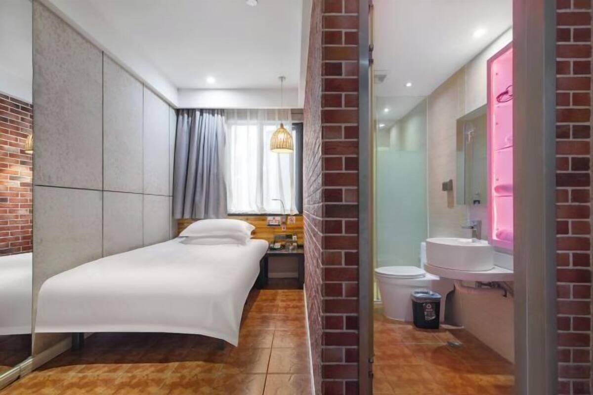 A hotel room with a bed, a nightstand, a bathroom with a sink and mirror, and a window with curtains.