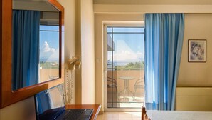 A hotel room with a bed, a laptop on a desk, a phone, and a view of a balcony with chairs. - Hotel Fotini (Kalamata)