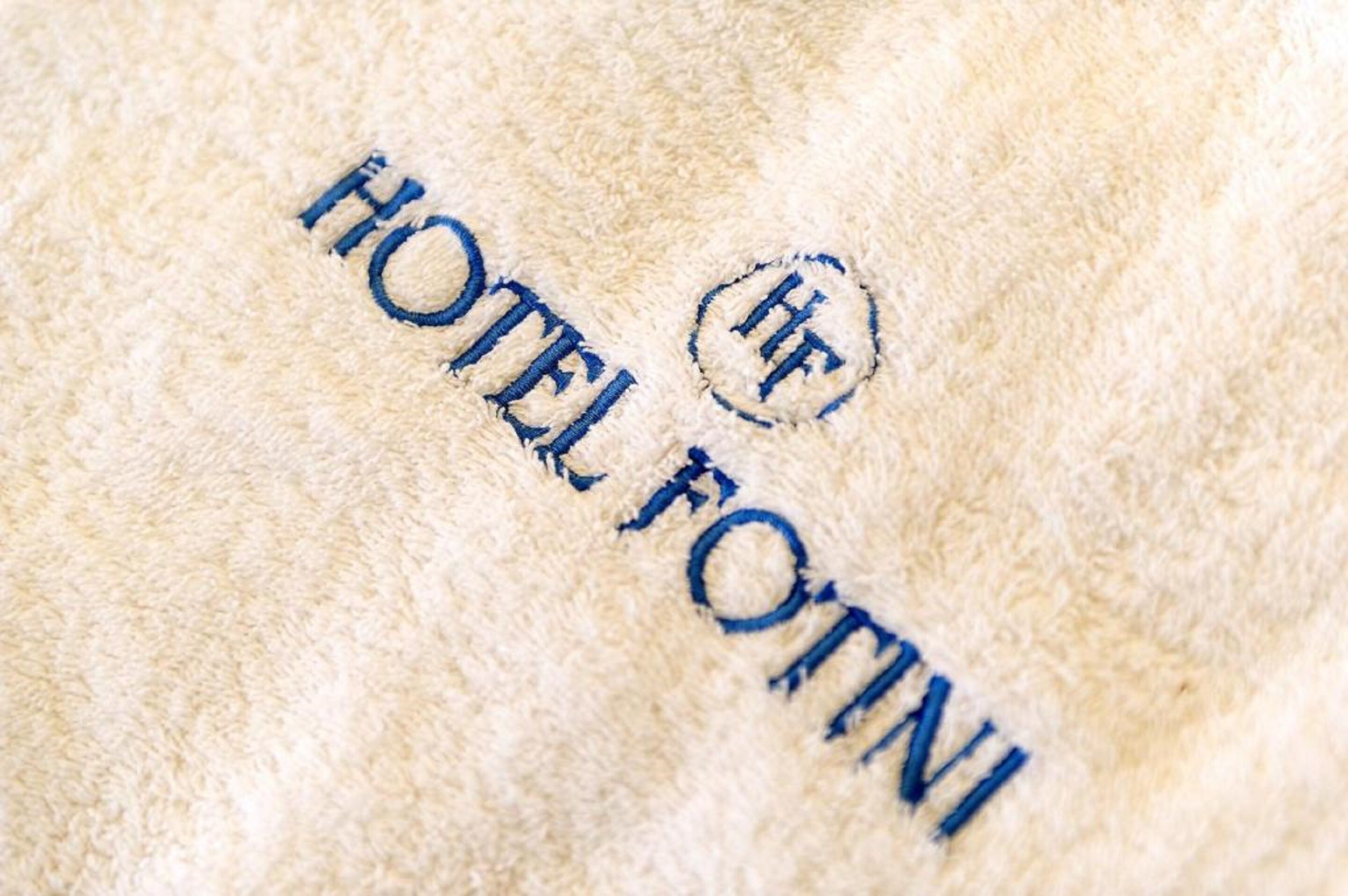 A close-up of a textured fabric with the words "HOTEL FOTINI" embroidered in blue thread.