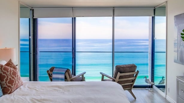 A bedroom with a large window overlooking the ocean, a bed, two chairs, and a small table. - WOW 10th Fl Corner Unit * Ocean Views * Pool + Hot Tub (San Diego)