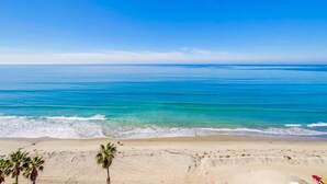 A beach with clear blue water, sandy shore, and palm trees. - WOW 10th Fl Corner Unit * Ocean Views * Pool + Hot Tub (San Diego)