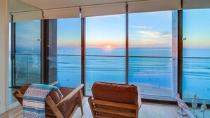 A balcony with a view of the ocean at sunset, featuring two leather chairs and a small table with a blanket. - WOW 10th Fl Corner Unit * Ocean Views * Pool + Hot Tub (San Diego)