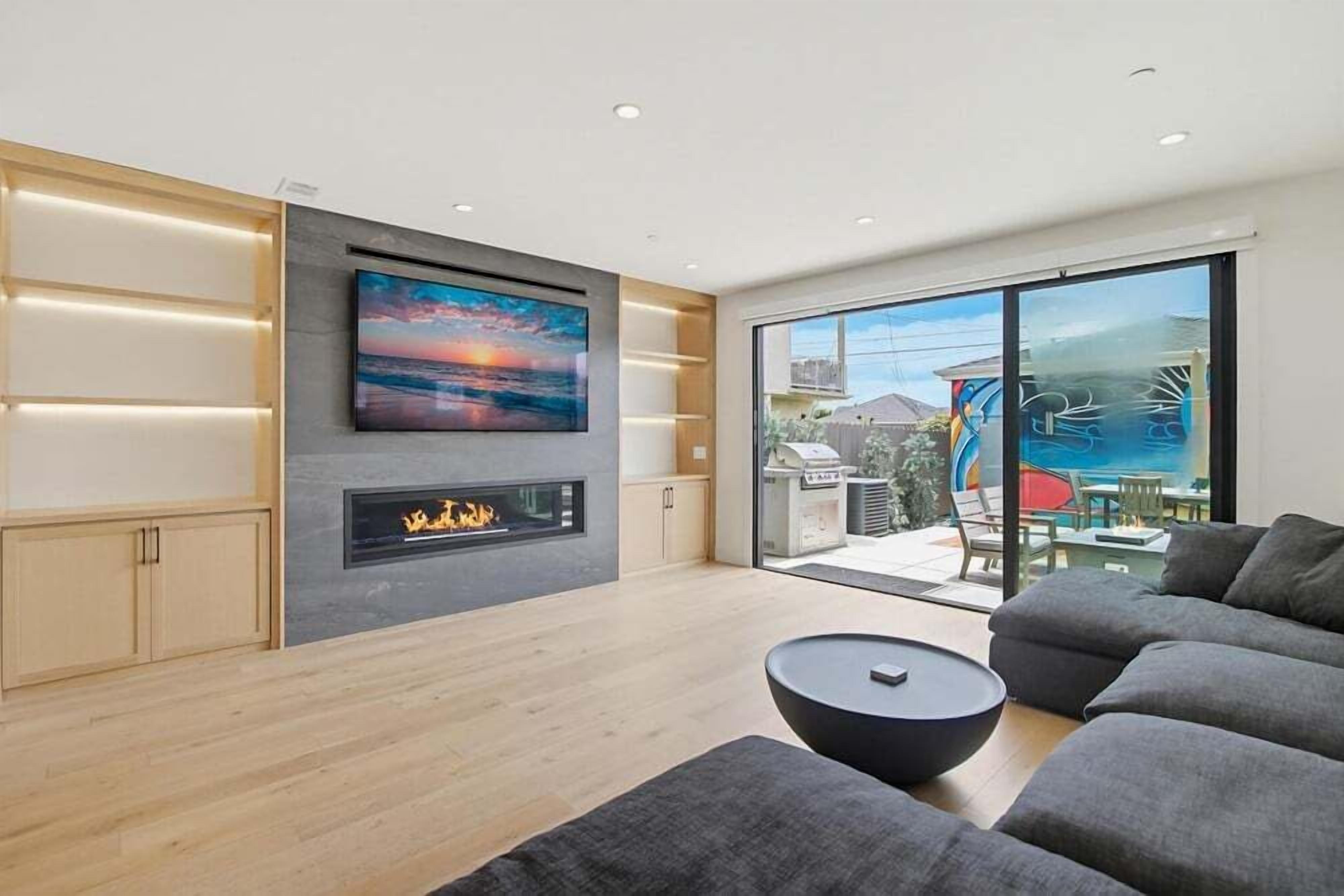 A modern living room with a fireplace, a large TV, and a balcony with a view.