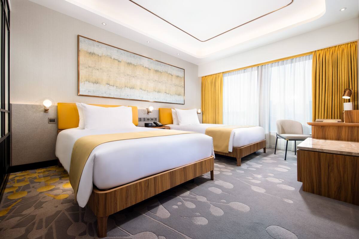 Ett hotellrum med två sängar, ett skrivbord, en stol och en stor, abstrakt målning på väggen.