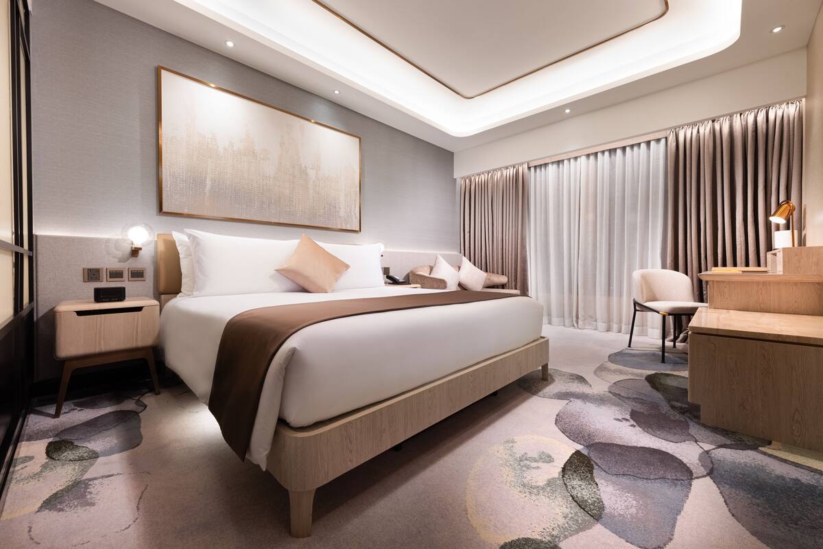 Ett modernt hotellrum med en stor säng, sängbord, ett skrivbord och ett stort fönster med gardiner.