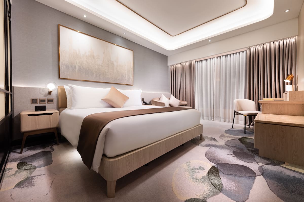 Ett modernt hotellrum med en stor säng, sängbord, ett skrivbord och ett stort fönster med gardiner.
