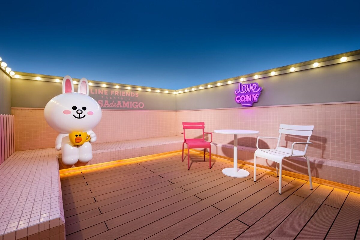 A cozy outdoor seating area with a neon sign, a large plush toy, and a tiled wall.