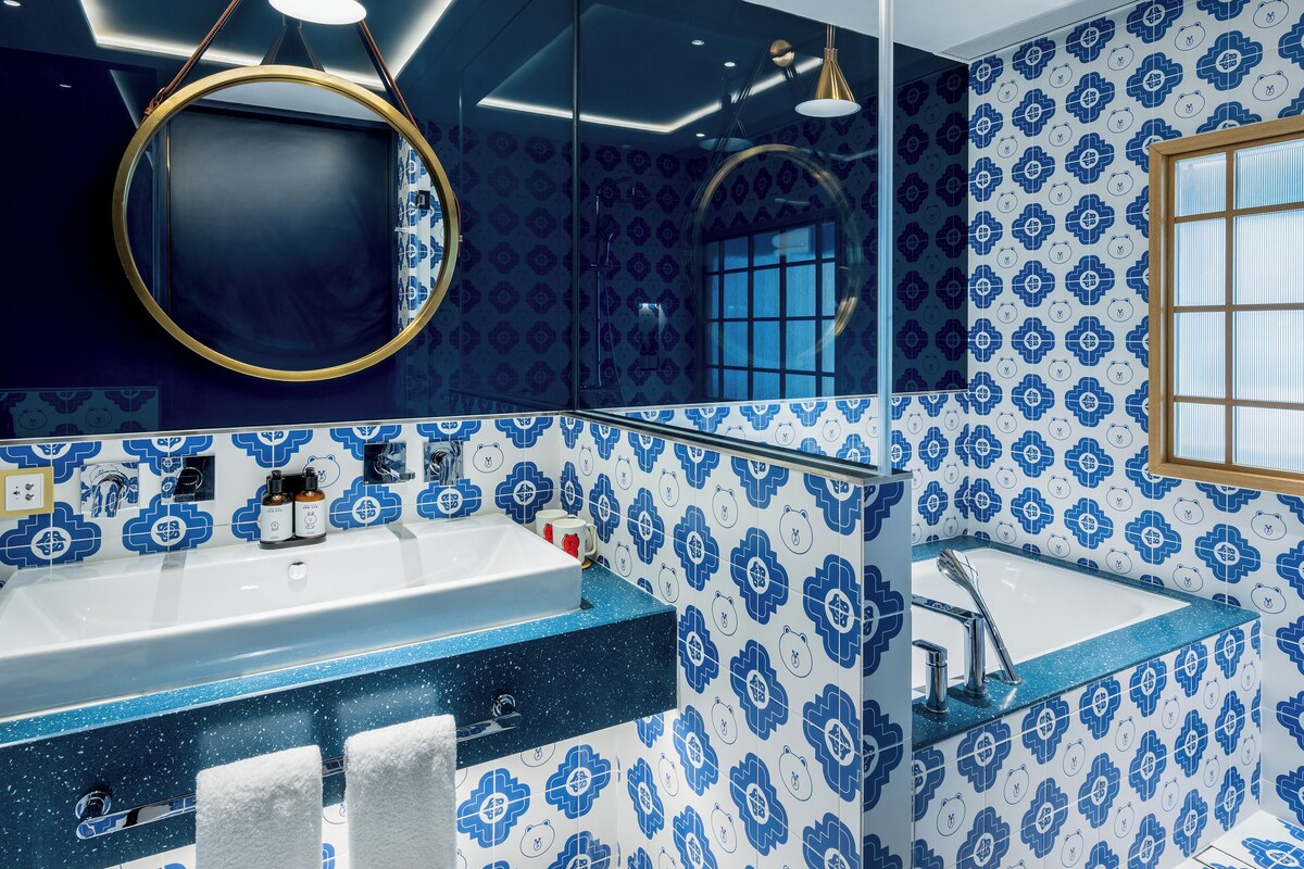 A bathroom with a blue and white floral tile pattern, a round mirror, and a modern light fixture.