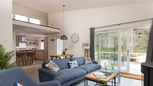 A modern living room with a blue sofa, a wooden coffee table, and a dining area with a kitchen in the background.
