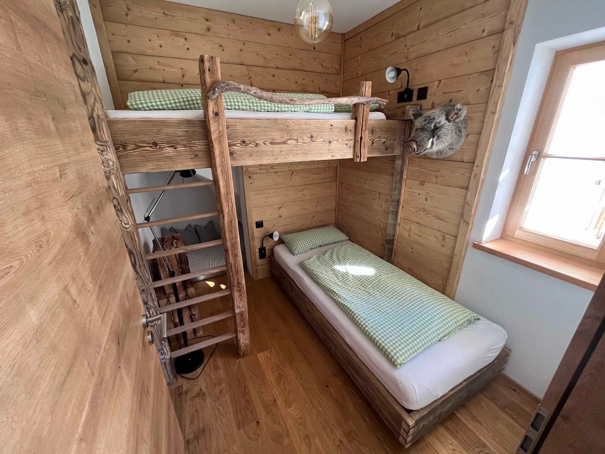Ein Zimmer mit einem hölzernen Etagenbett, einer Leiter, einem kleinen Fenster und einer Lampe.