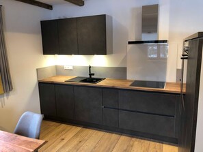 A modern kitchen with dark cabinets, a wooden countertop, a black sink, and a built-in stove.