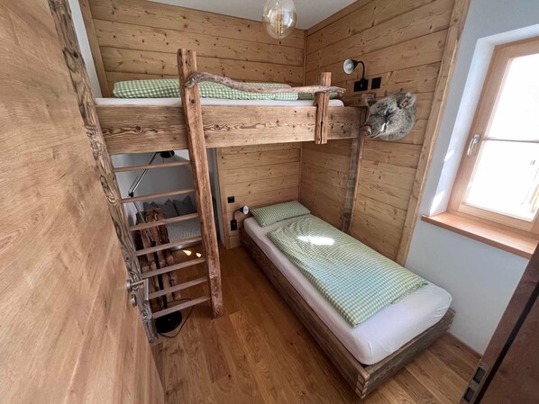 A wooden bunk bed room with a ladder, a small desk, and a window.