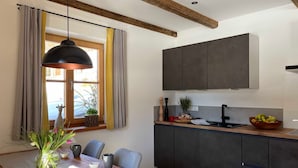 Une cuisine moderne avec des meubles de couleur sombre, une table à manger en bois et un luminaire suspendu.