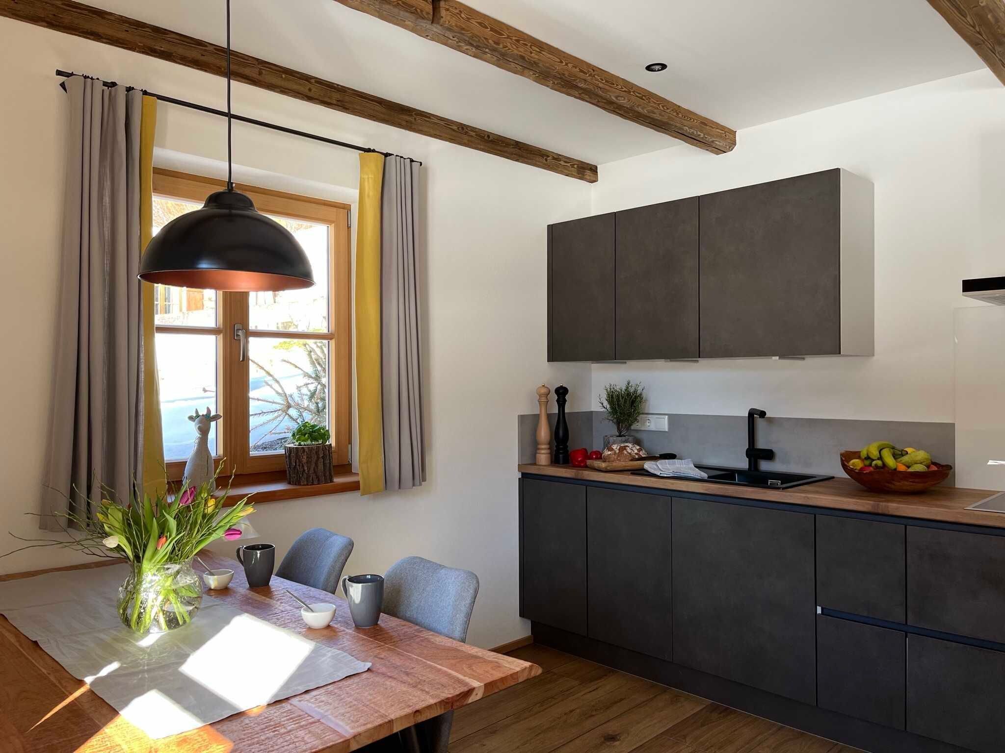 Eine moderne Küche mit dunklen Schränken, einem Holztisch und einer hängenden Pendelleuchte.