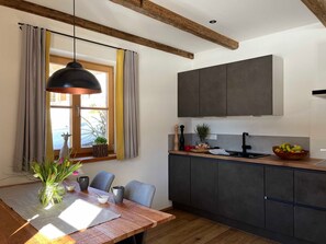 A modern kitchen with dark cabinets, a wooden dining table, and a hanging pendant light. - Sunnseitn, Germany (Bayrischzell)
