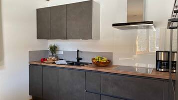 A modern kitchen with dark cabinets, a wooden countertop, a stainless steel range hood, and a coffee maker.